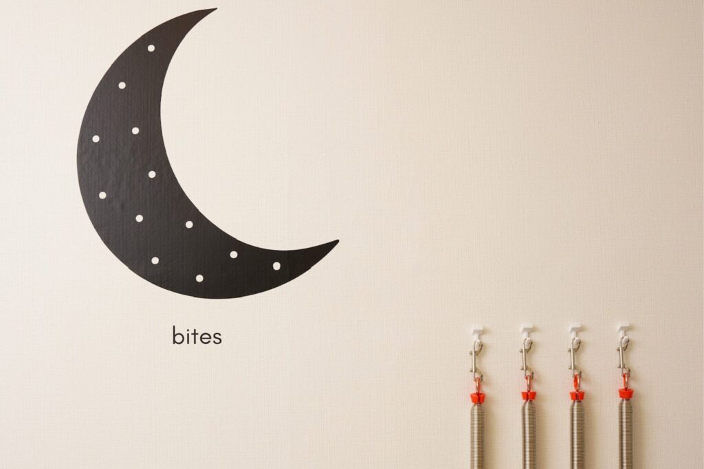 壁に描かれた三日月と「bites」のロゴ、隣にはピラティスマシン用のスプリングが4本掛けられている