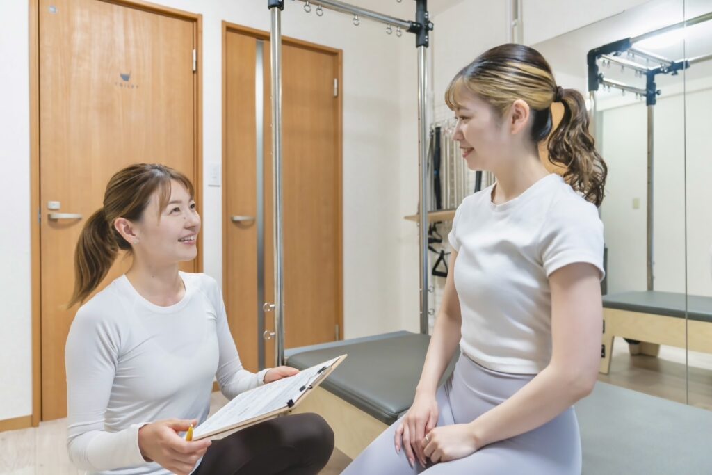 ピラティスセッション前にインストラクターと受講者が笑顔でカウンセリングしている場面